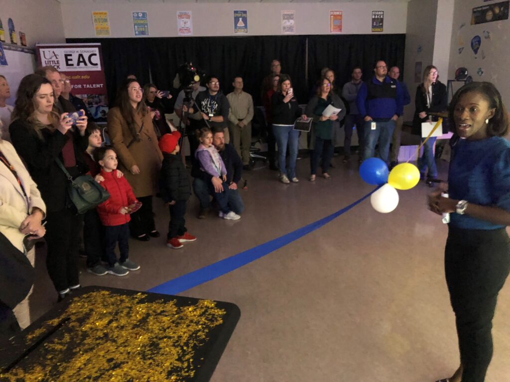 A woman talks to a group of people standing to the left of her.